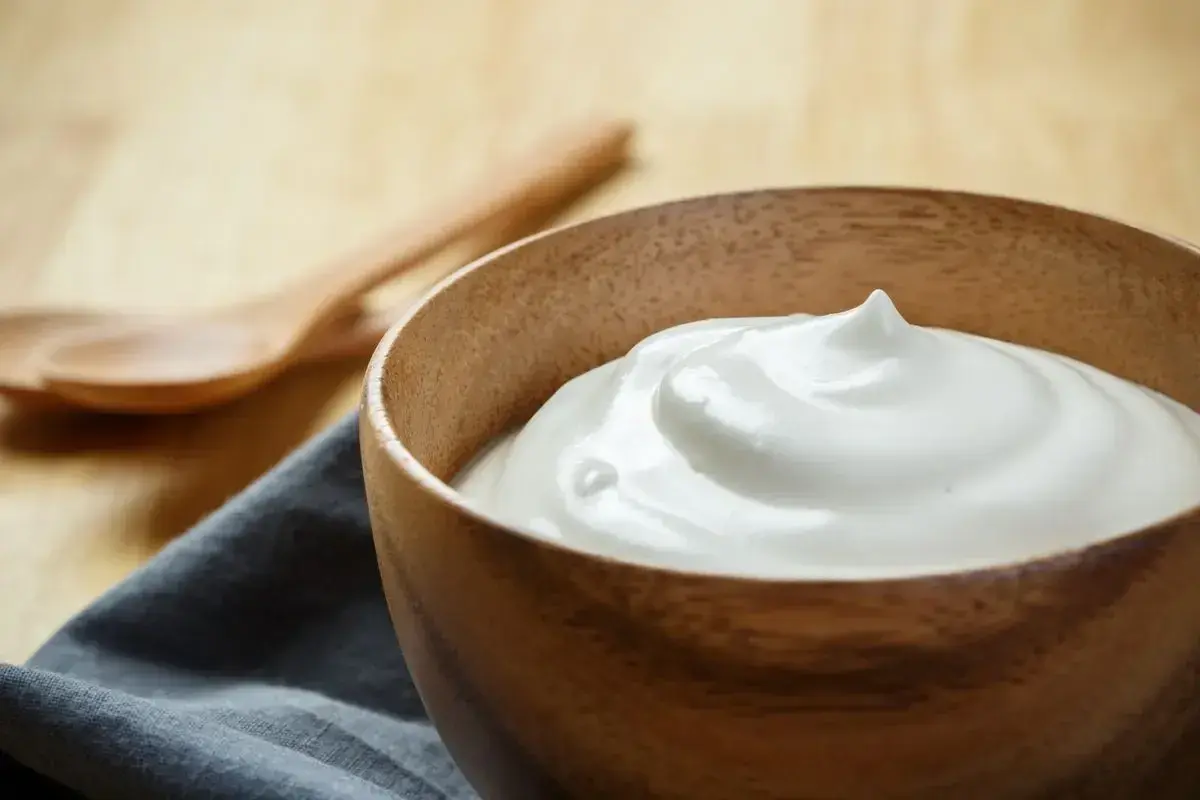 Una ciotola di legno contiene una soffice crema al latte, pronta per essere gustata. Due cucchiai di legno sono sullo sfondo.