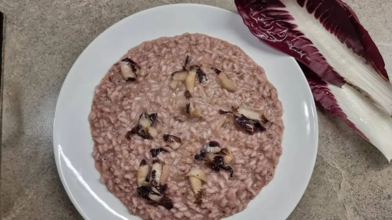 Un cremoso risotto al radicchio rosso, con pezzetti di verdura che spuntano. Accanto, una foglia di radicchio fresco.