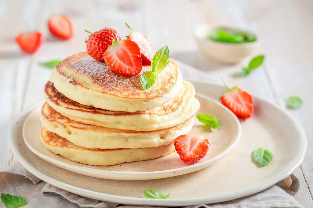 Pancake allo yogurt soffici e dorati, guarniti con fragole fresche e zucchero a velo. Un dolce inizio di giornata.