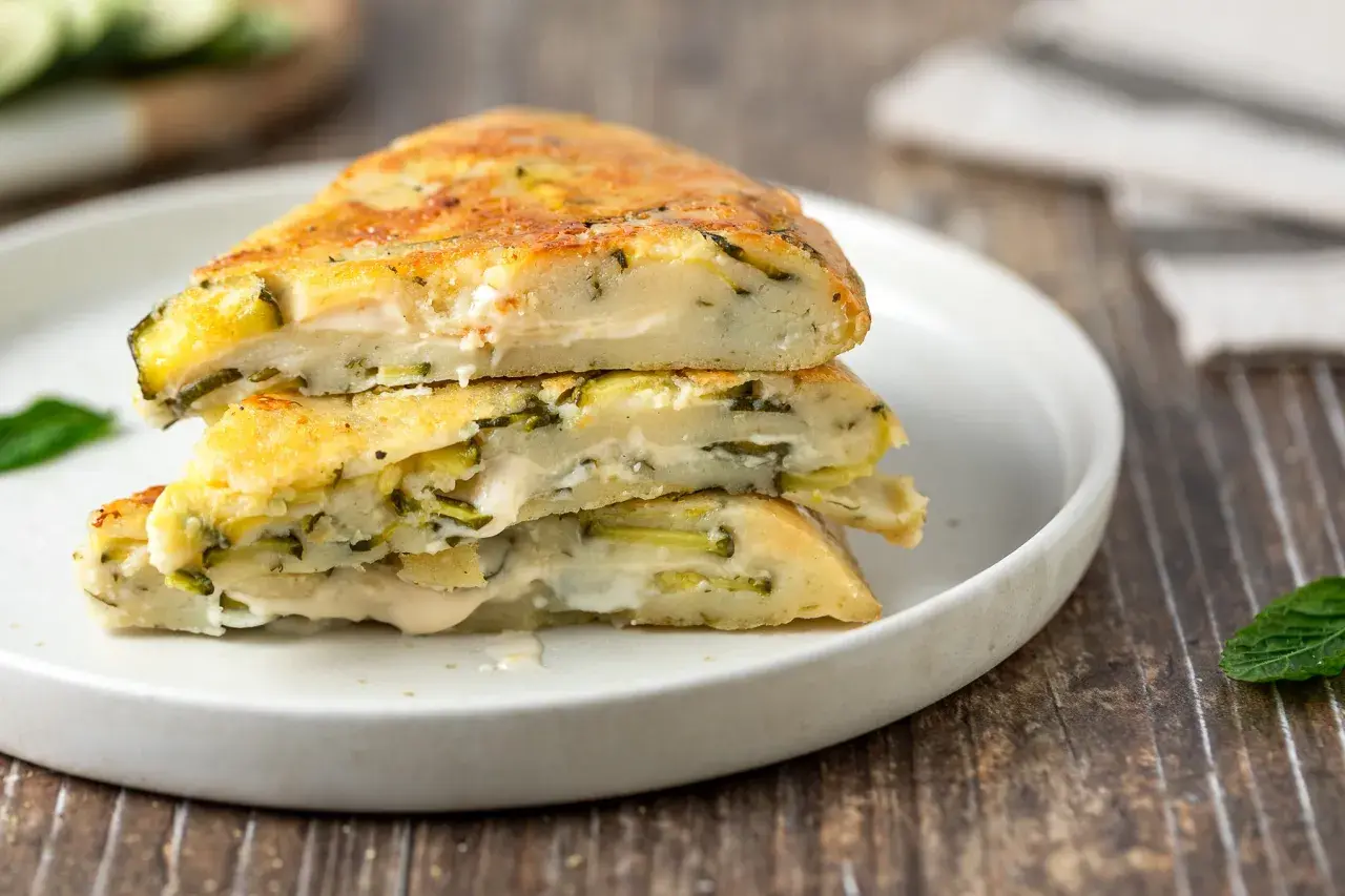 Fette di torta salata con zucchine e formaggio, impilate su un piatto bianco.