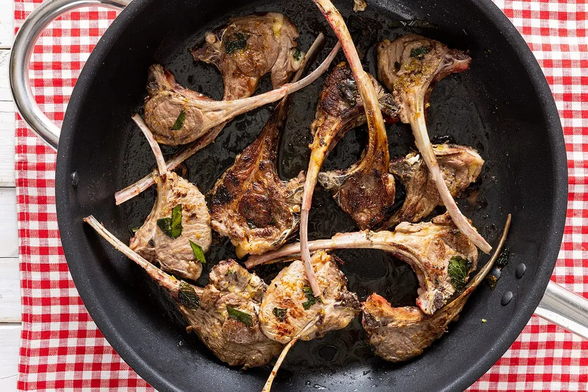 Costine di agnello in padella, dorate e succulente, pronte per essere gustate.