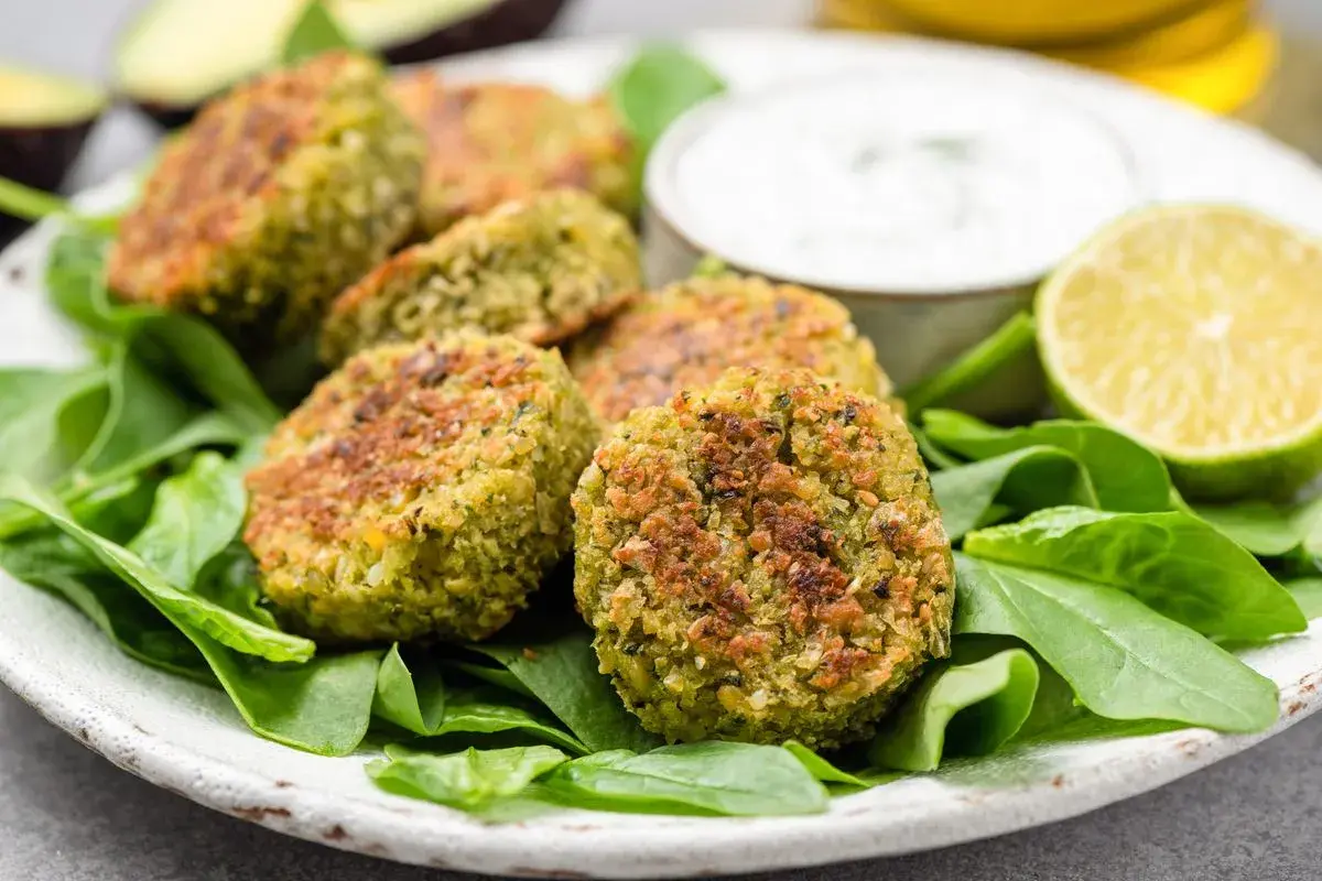 Polpette di spinaci dorate su un letto di spinaci freschi, con una ciotola di salsa e spicchi di lime.