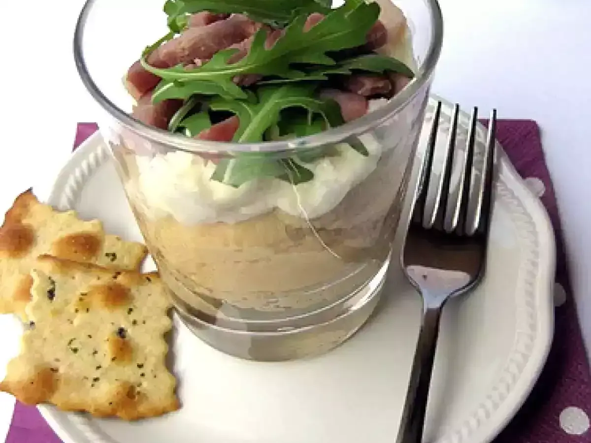 Deliziosa crema di ceci in bicchiere, stratificata con formaggio spalmabile e guarnita con rucola e prosciutto. Servita con cracker croccanti.