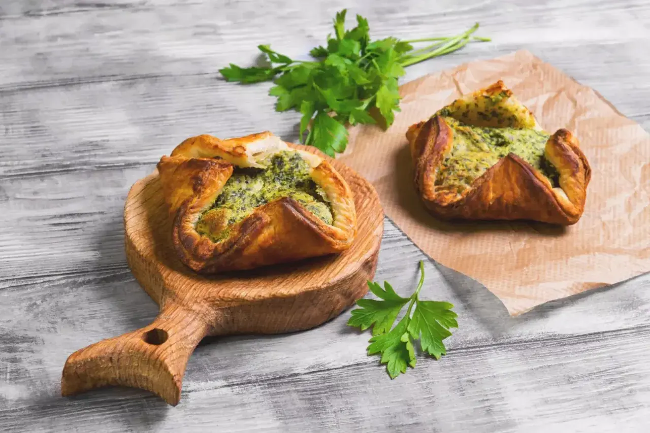 Due fagottini di pasta sfoglia con ripieno verde, uno su tagliere di legno, l'altro su carta forno. Idee su pasta sfoglia cosa mettere dentro.