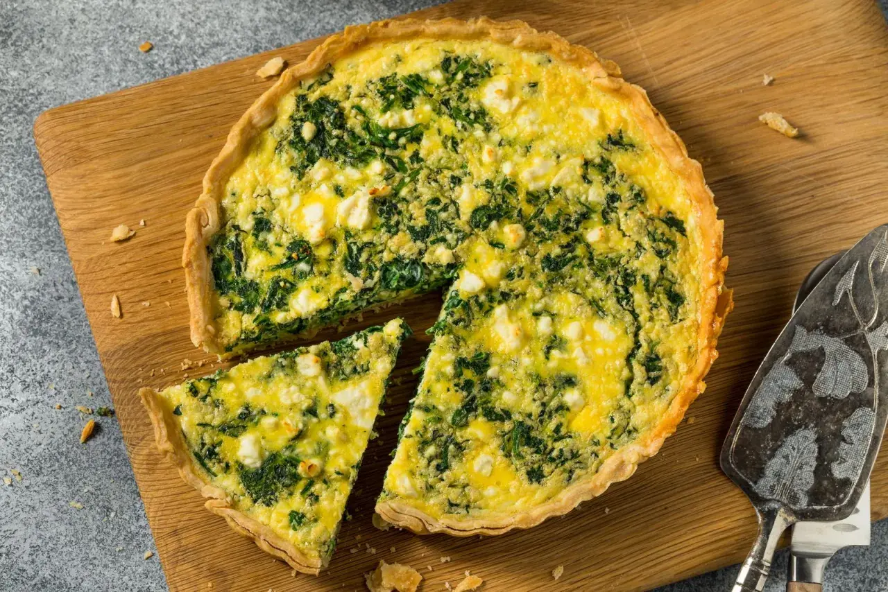 Torta salata ricotta e spinaci dorata e invitante, con una fetta tagliata su un tagliere di legno.
