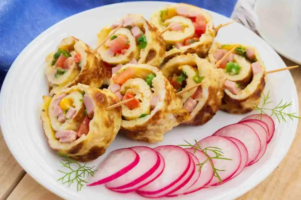 Rotolo di frittata ripieno di prosciutto, pomodoro e verdure, servito con fettine di ravanello.
