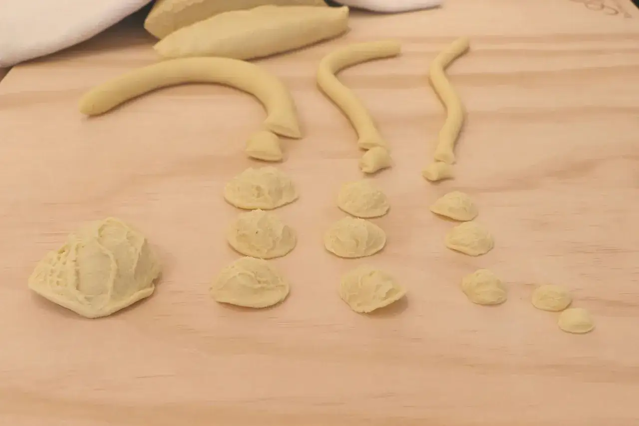 Orecchiette fatte in casa in varie fasi di preparazione, disposte su un tagliere di legno.