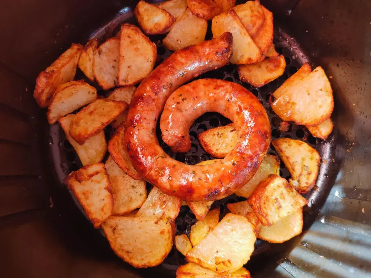 Salsiccia arrotolata e patate croccanti appena sfornate dalla friggitrice ad aria.