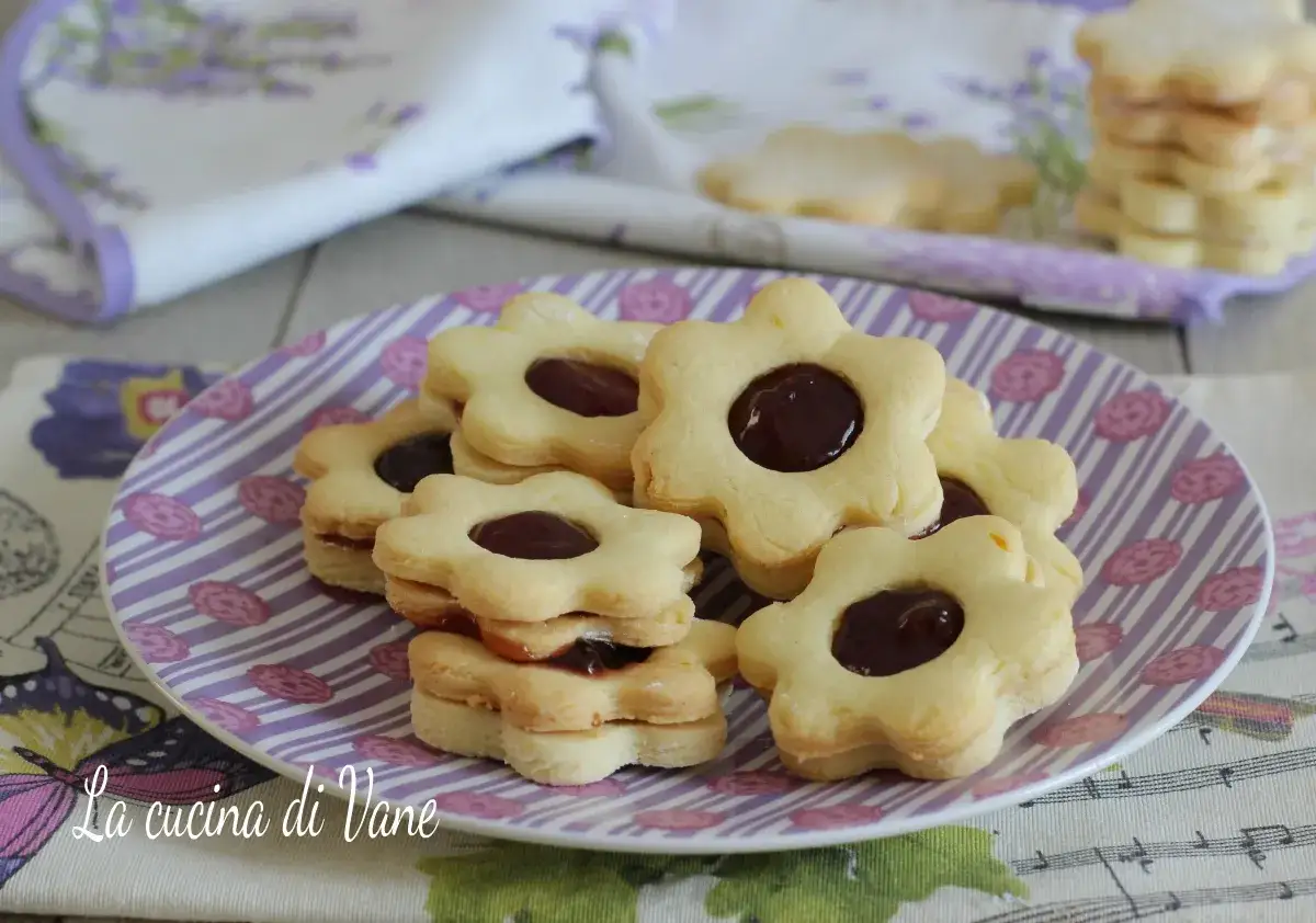 Biscotti con marmellata a forma di fiore, impilati su un piatto a righe viola. Deliziosi dolcetti fatti in casa.