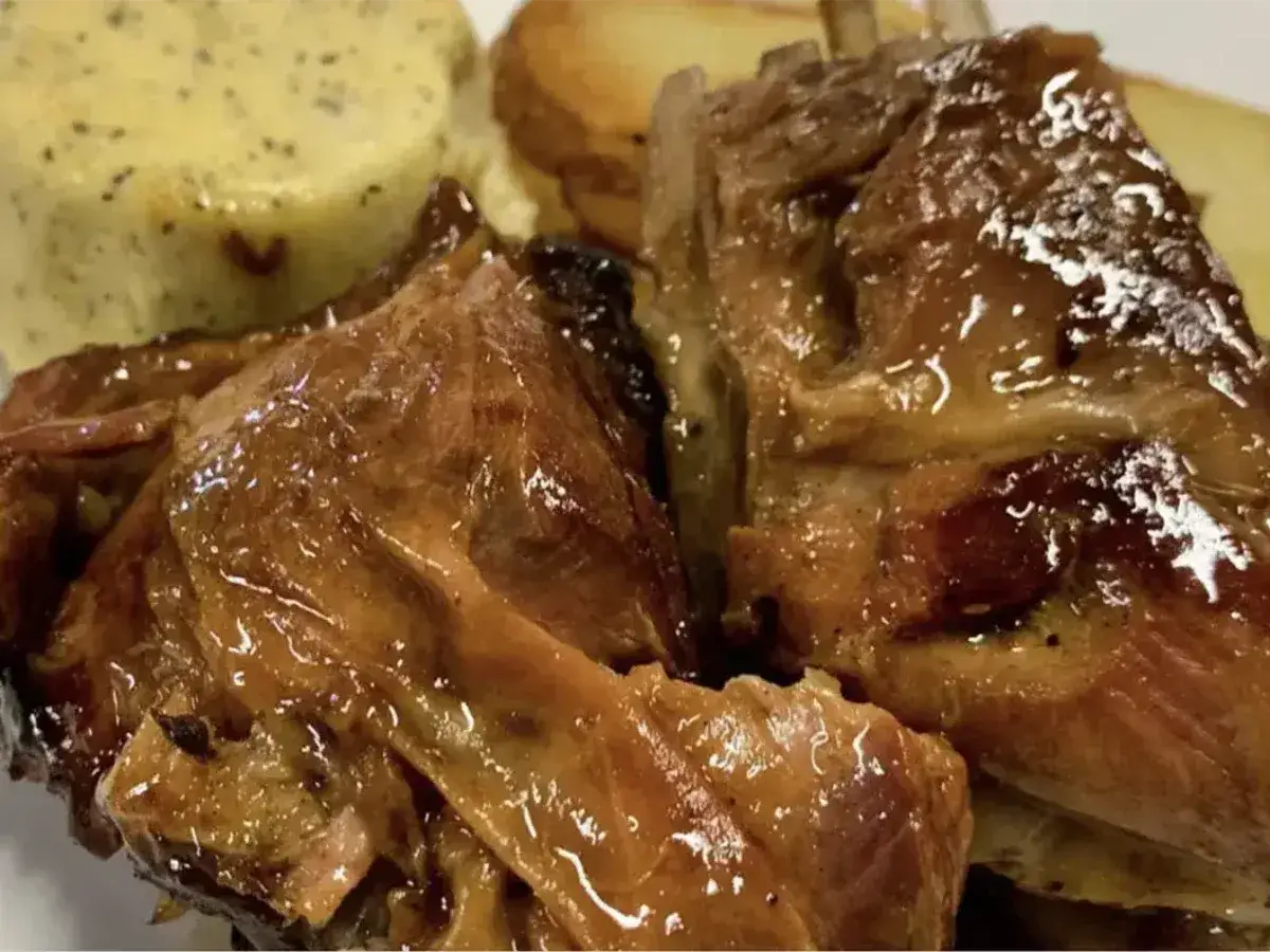 Succulento agnello al forno, dorato e lucido, servito con patate arrosto e una crema di verdure. Un piatto invitante e saporito.