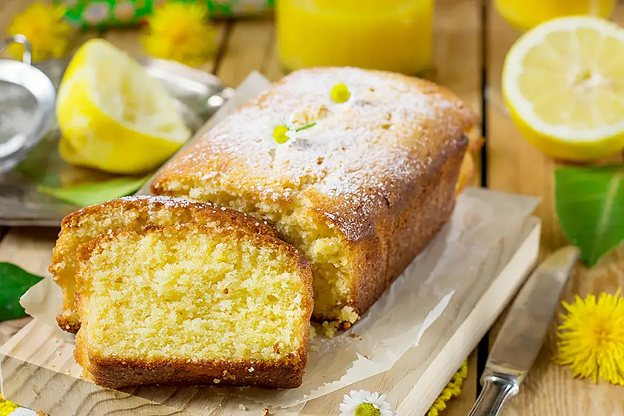 Un soffice plumcake al limone, spolverato di zucchero a velo e decorato con fiori, pronto per essere gustato.