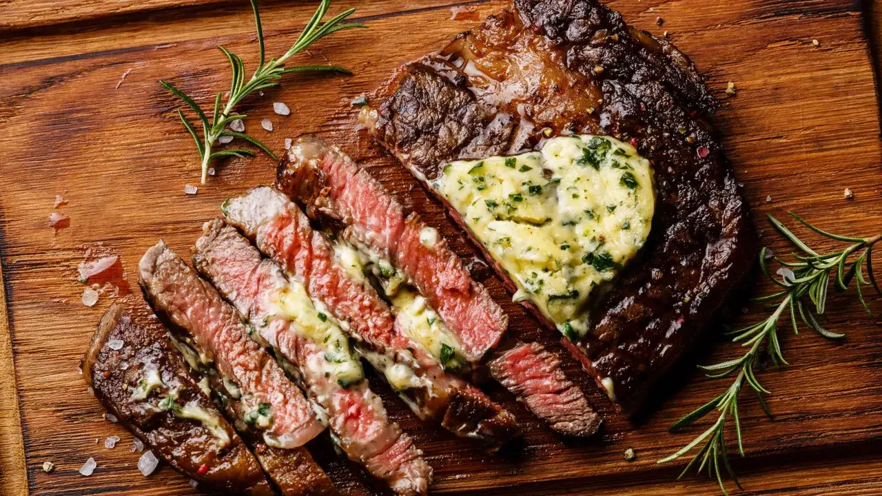 Costata di manzo succulenta, affettata e condita con burro alle erbe, su tagliere di legno con rosmarino e sale grosso.