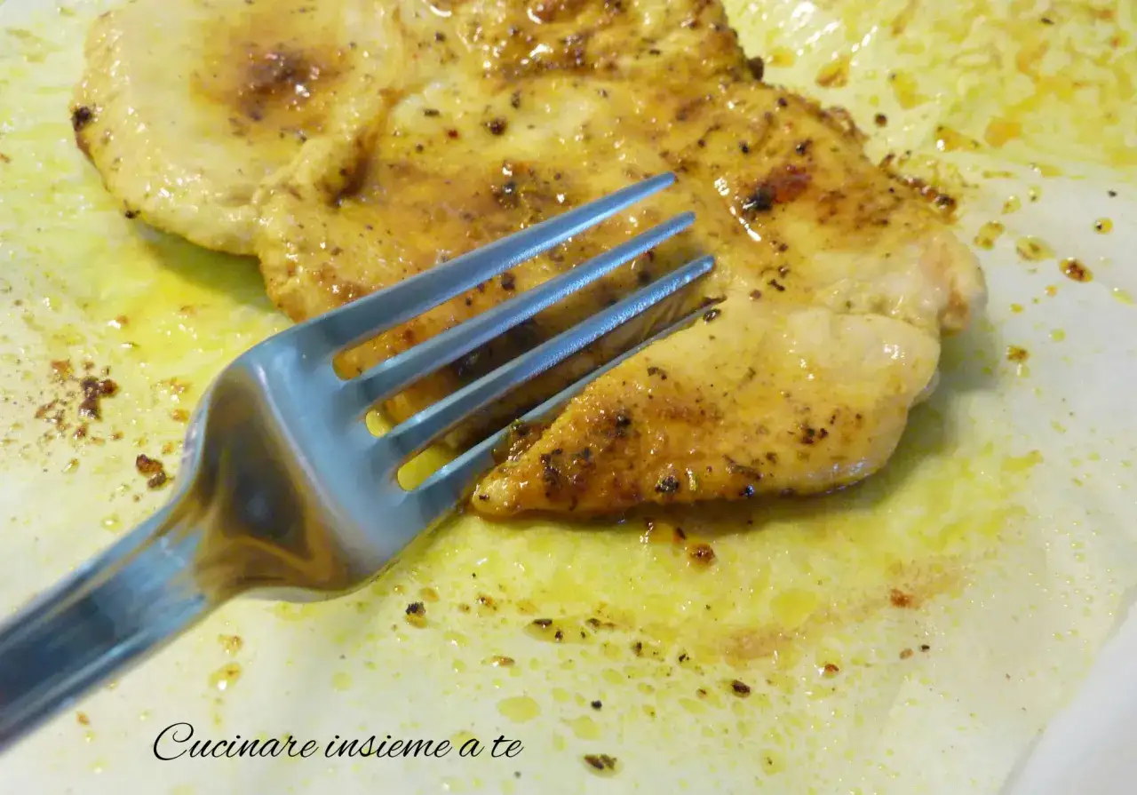 Un succulento petto di pollo in padella, dorato e speziato, pronto per essere gustato con una forchetta.