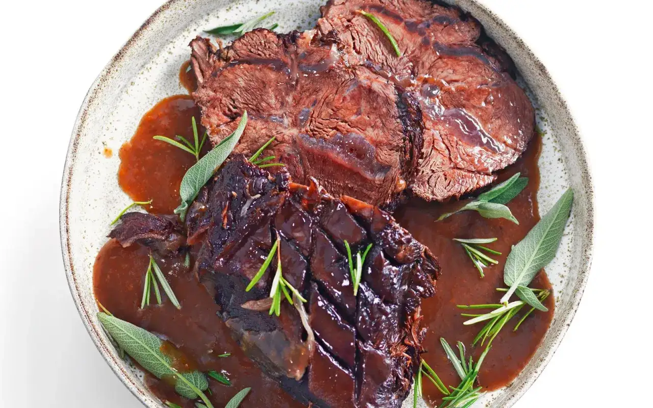 Succulento brasato di manzo, tenero e saporito, nappato con salsa scura e guarnito con rosmarino e salvia.