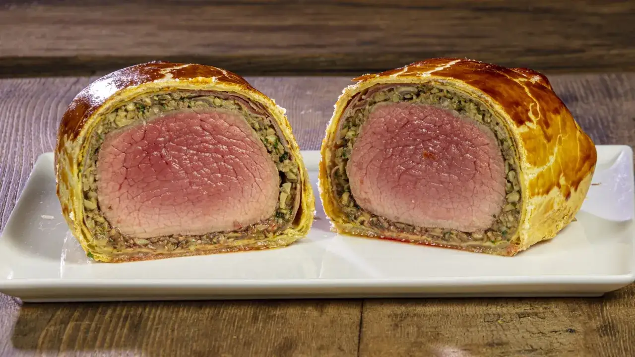 Un succulento filetto alla Wellington, tagliato a met&agrave;, rivela la carne rosata e il ricco ripieno di funghi, avvolti in una sfoglia dorata.