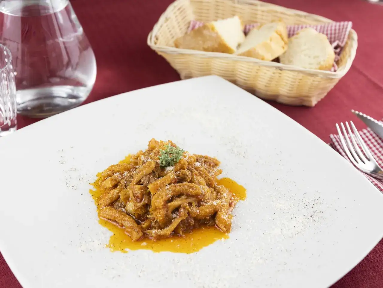 Un piatto di trippa alla fiorentina fumante, guarnito con erbe fresche e parmigiano, pronto per essere gustato con pane fresco.