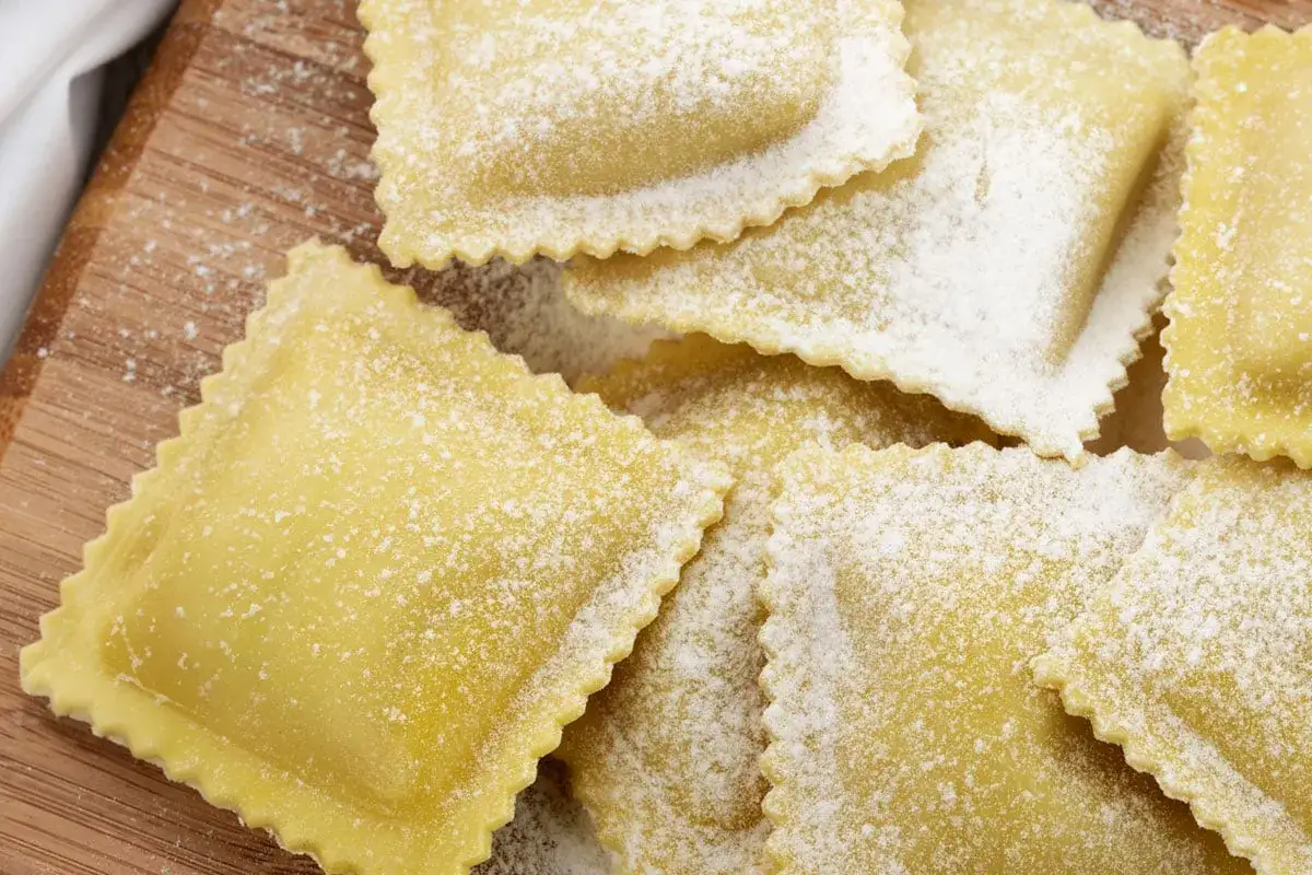 Ravioli quadrati fatti in casa, spolverati di farina, pronti per il ripieno.