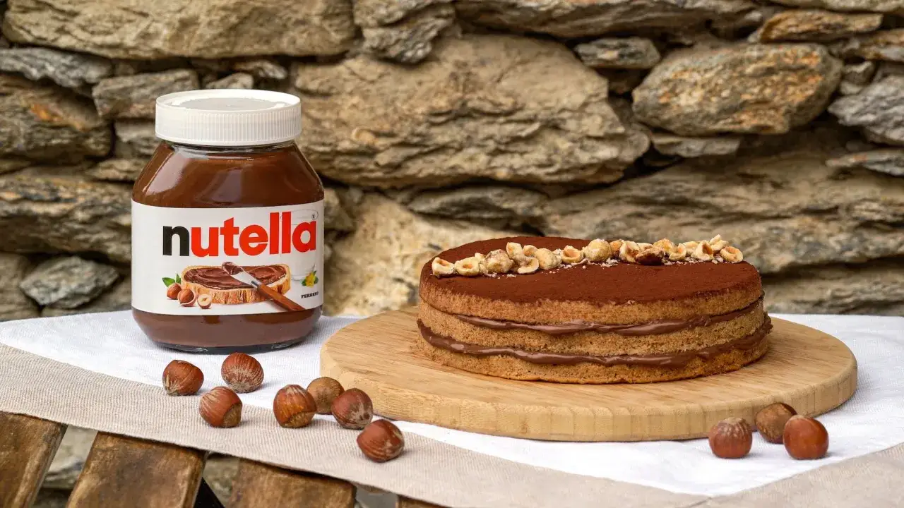 Un goloso cheesecake alla nutella, decorato con nocciole tostate, accanto a un barattolo della crema spalmabile.