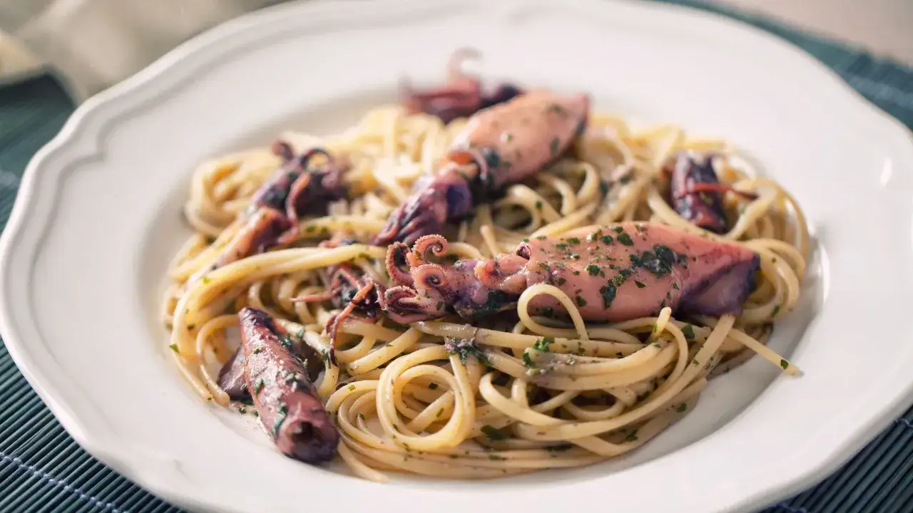 Spaghetti con calamari freschi, un piatto di mare saporito e profumato, guarnito con prezzemolo tritato.