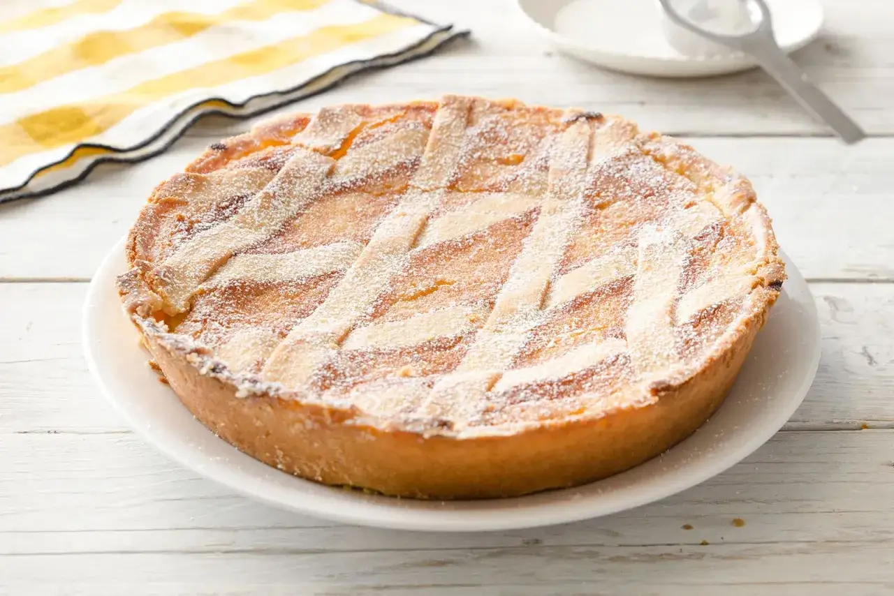 Pastiera giallo zafferano, con la sua crosta dorata e la decorazione a griglia, spolverata di zucchero a velo.