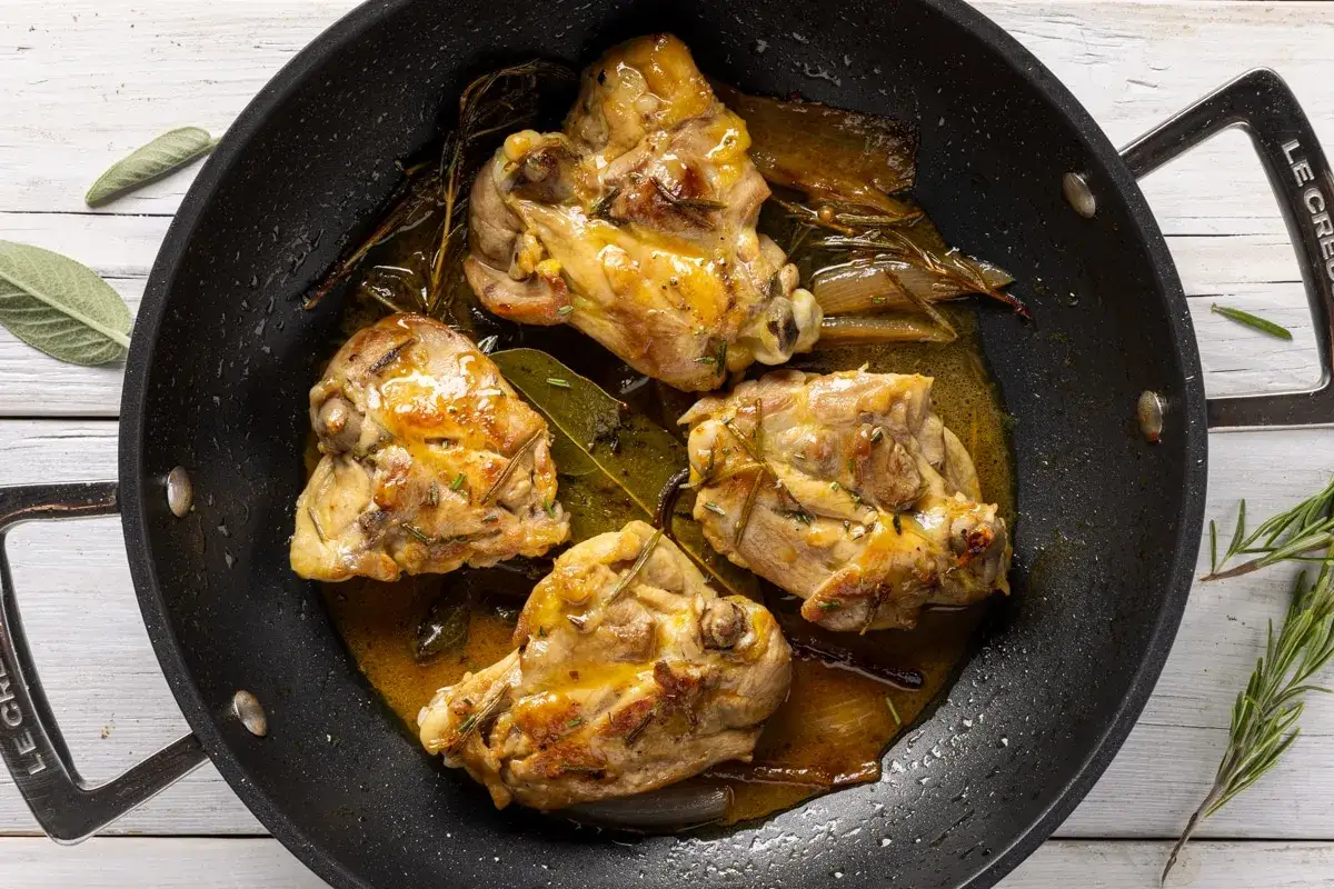 Cosce di pollo in padella, dorate e succulente, con erbe aromatiche e un sugo invitante.