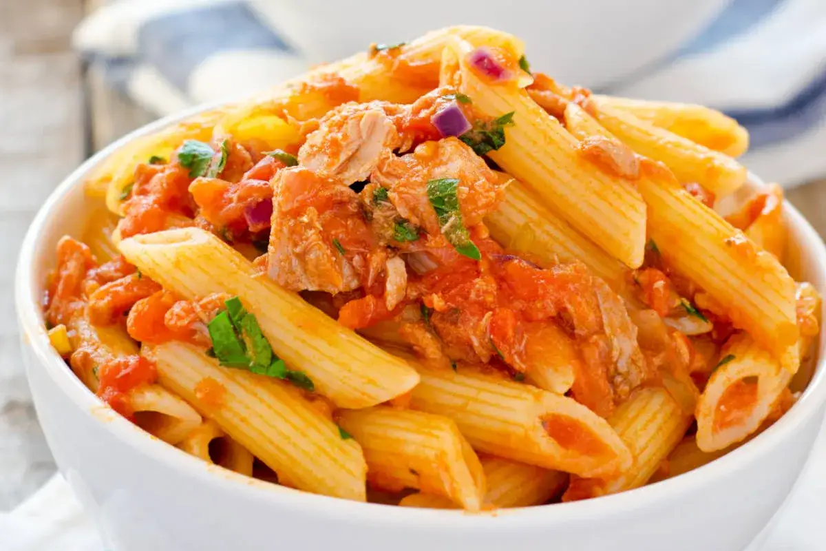Penne al tonno in una ciotola bianca, condite con sugo di pomodoro, tonno e prezzemolo fresco. Un piatto semplice e gustoso.