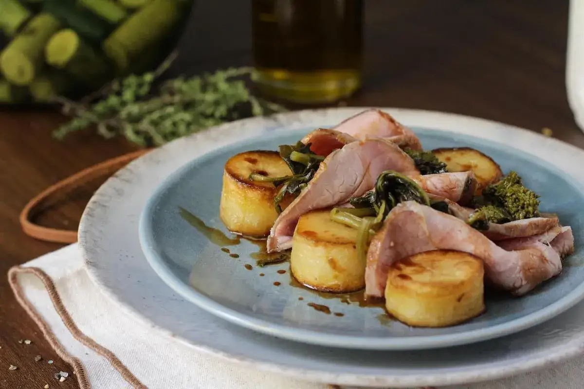 Delizioso arrosto di manzo affettato con patate arrosto e verdure verdi su un piatto blu.