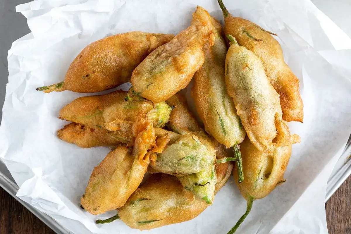 Un mucchio di croccanti fiori di zucca ripieni, dorati e invitanti, adagiati su carta bianca.