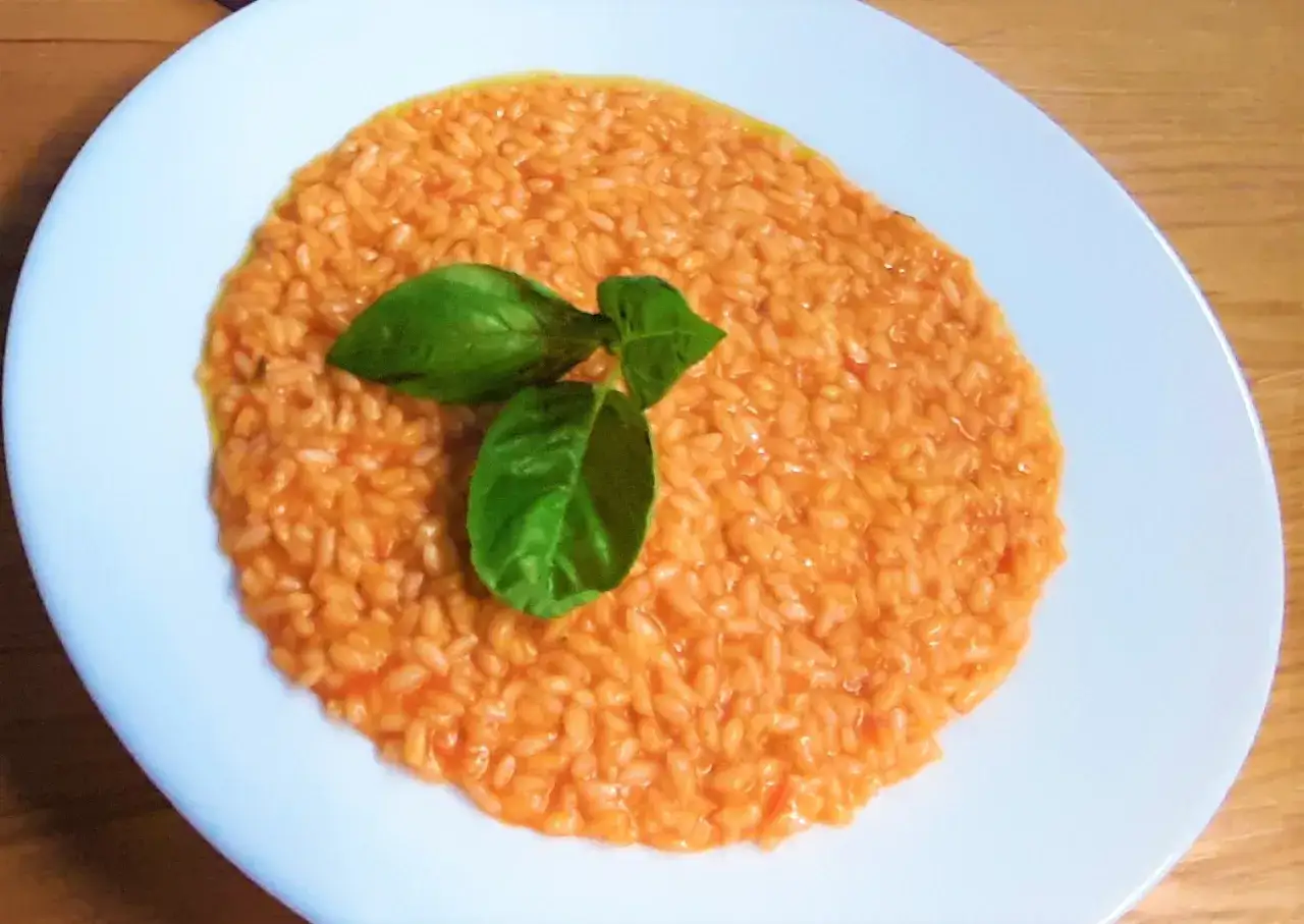 Un cremoso riso al pomodoro, servito su un piatto bianco e guarnito con foglie di basilico fresco.