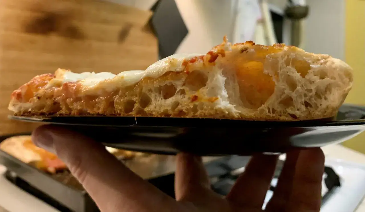 Fetta di pizza con crosta alveolata e mozzarella filante, un'esplosione di sapori che ricorda il giallo zafferano.