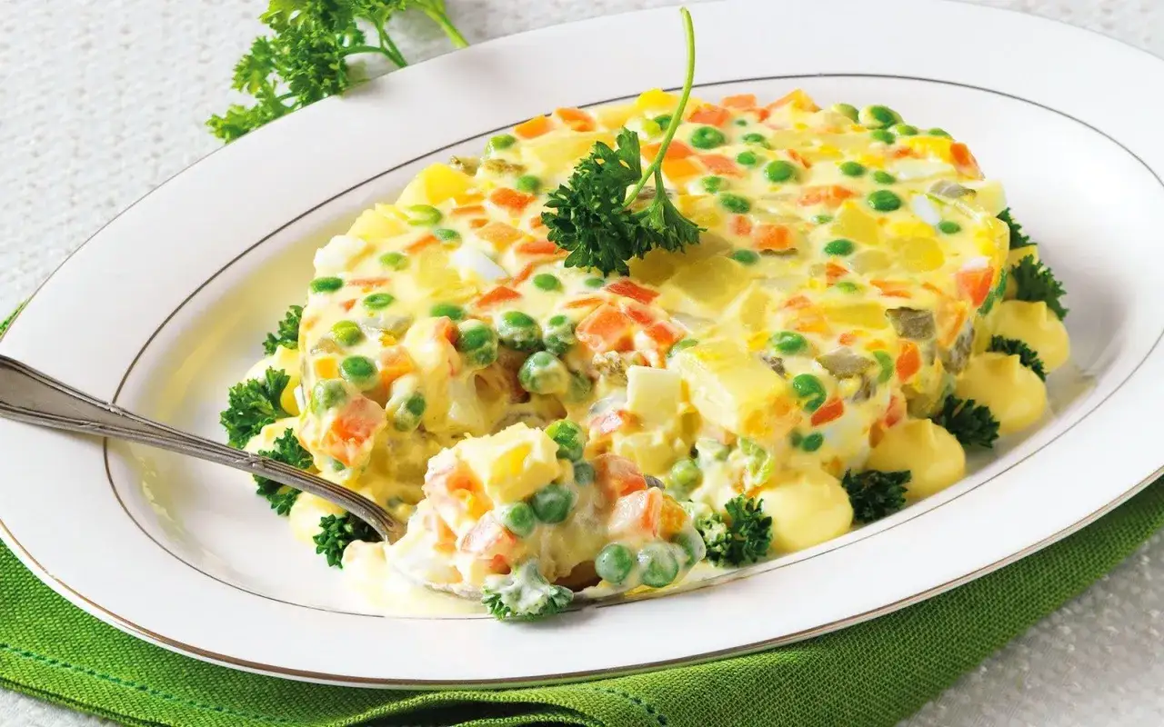 Insalata russa ricetta della nonna: un piatto cremoso con patate, piselli, carote e uova, guarnito con prezzemolo.