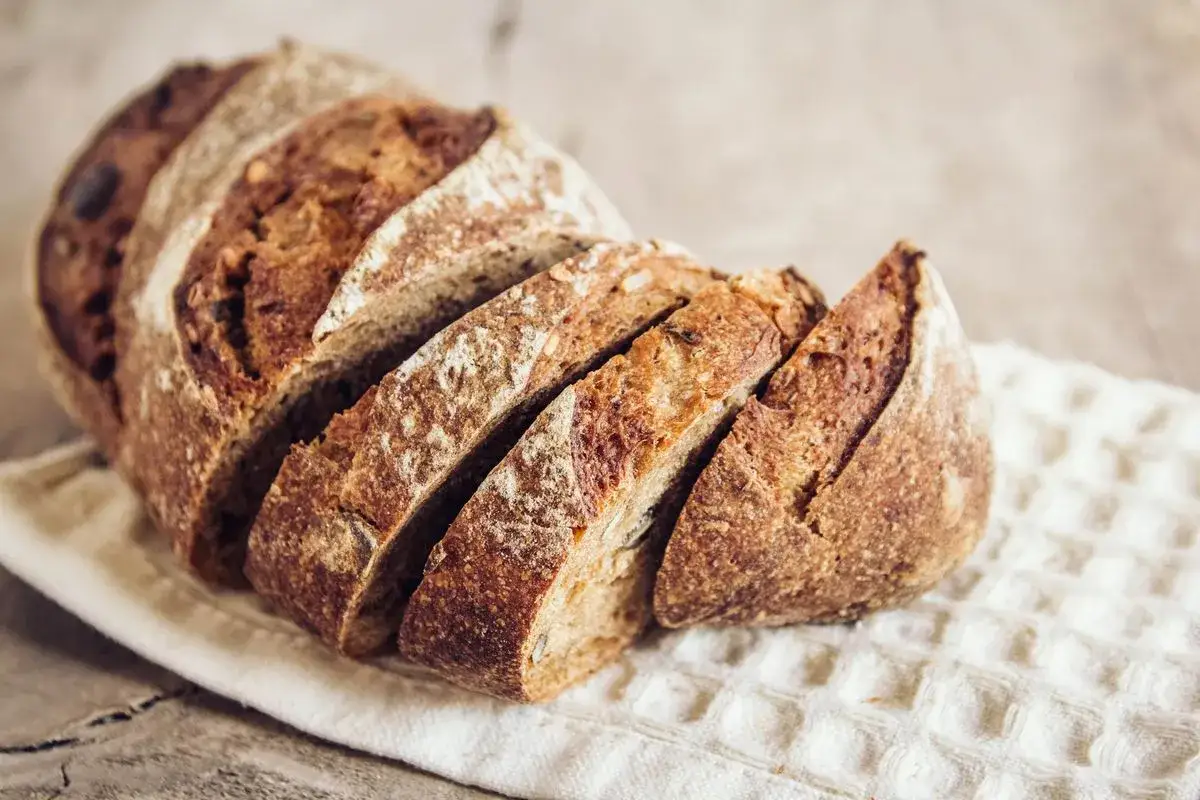 Fetta di pane di grano saraceno rustico, con crosta croccante e mollica scura e invitante, su un canovaccio bianco.