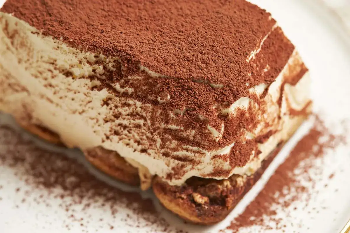 Un delizioso tiramis&ugrave; con uova pastorizzate, cosparso di cacao amaro, su un piatto bianco.