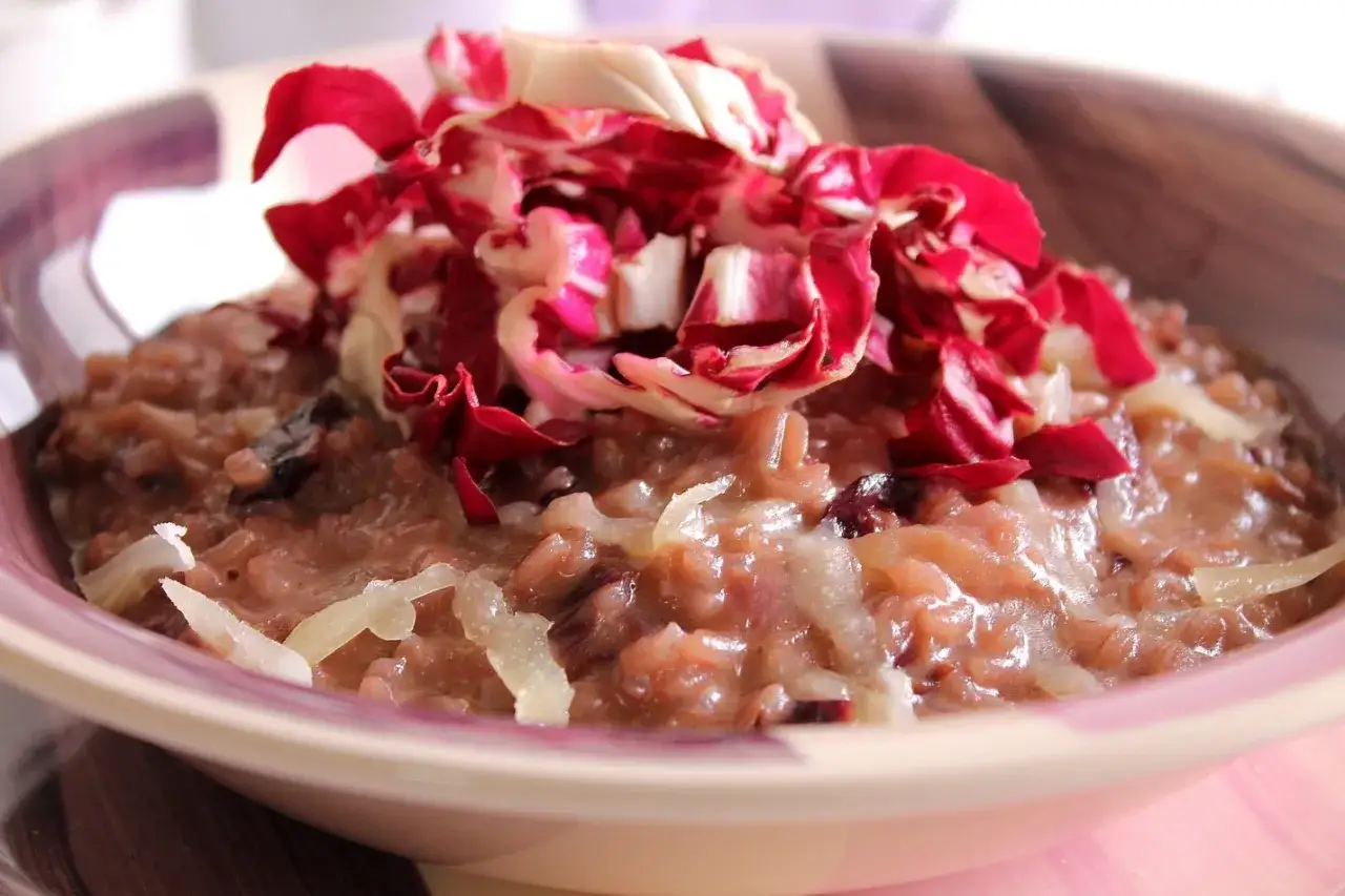 Un cremoso risotto al radicchio rosso, guarnito con scaglie di formaggio e foglie fresche di radicchio.