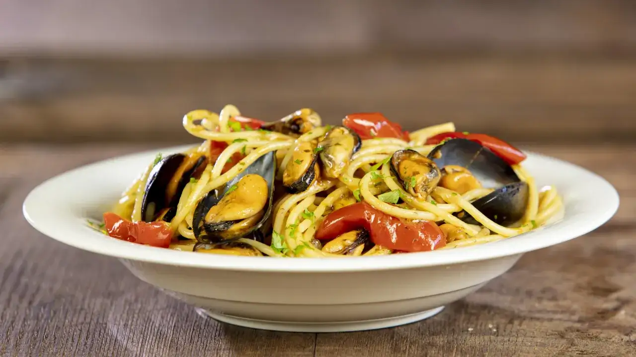 Un piatto invitante di pasta con le cozze, pomodorini e prezzemolo fresco su un tavolo di legno.