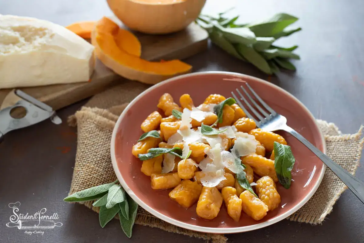 Gnocchi di zucca dorati, guarniti con parmigiano e foglie di salvia fresca, pronti per essere gustati.