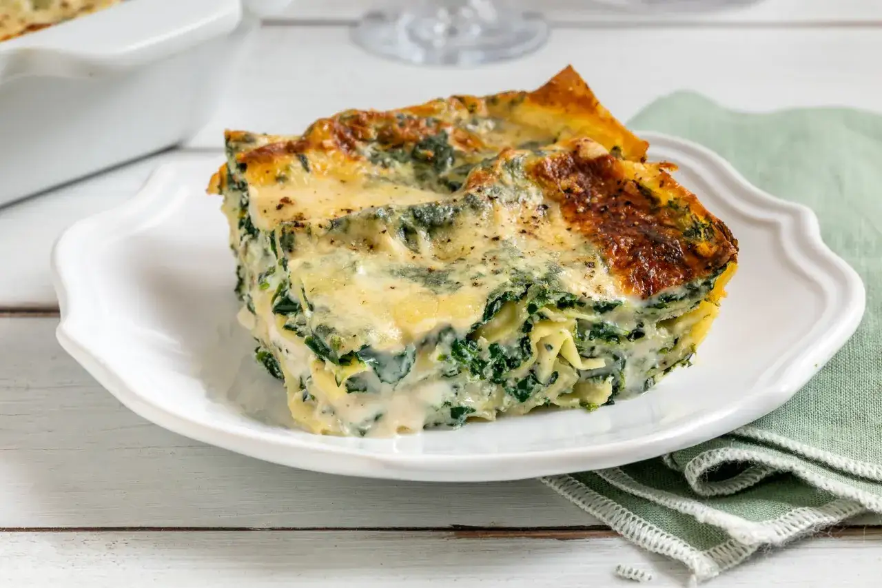 Una fetta di lasagne ricotta e spinaci, con strati di pasta, ripieno cremoso e crosticina dorata, servita su un piatto bianco.