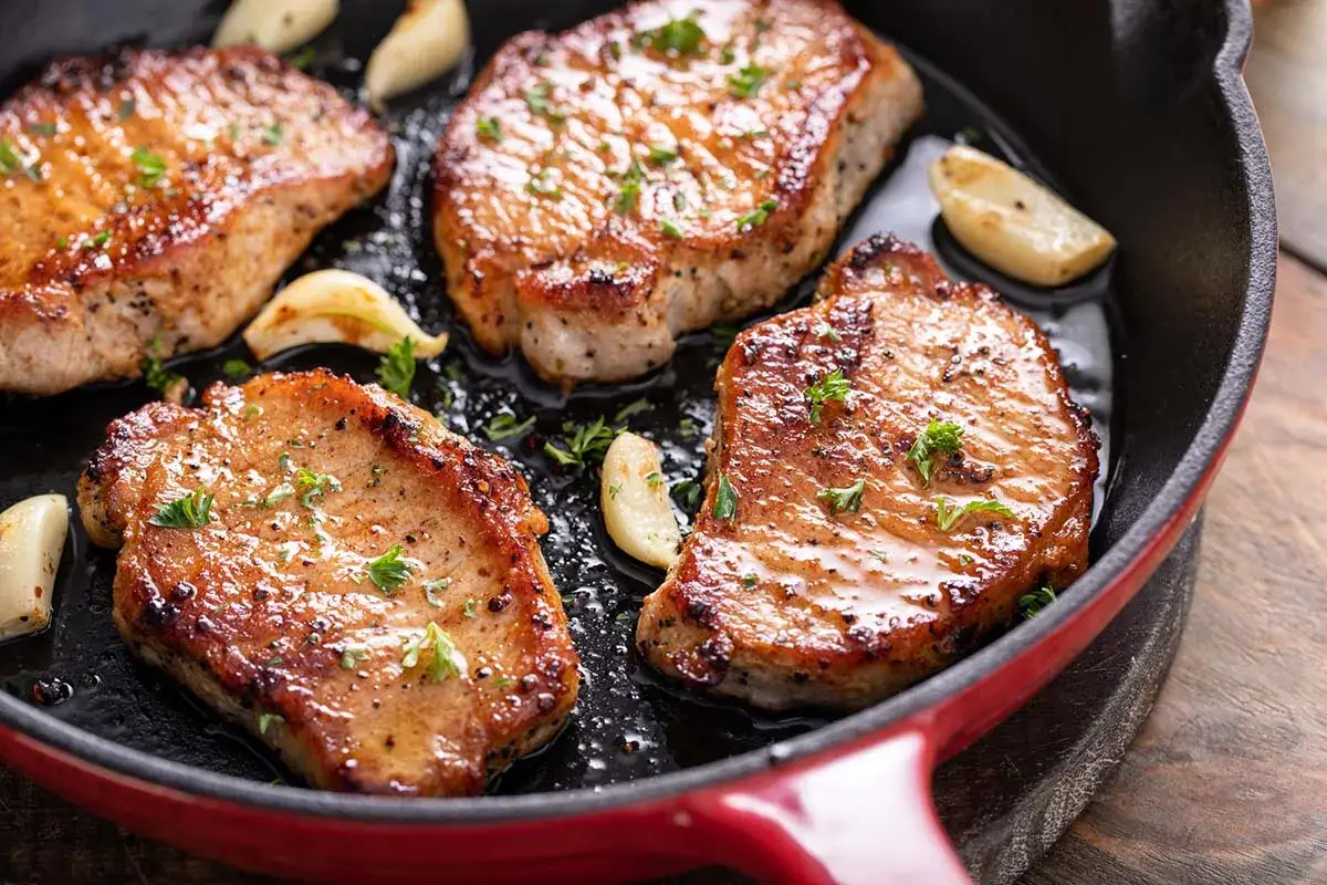 Quattro succulente fette di lonza di maiale in padella, dorate e profumate con aglio e prezzemolo.