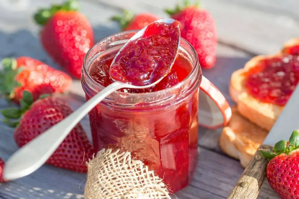 Un cucchiaio pieno di marmellata di fragole fatta in casa, accanto a un barattolo e fragole fresche.