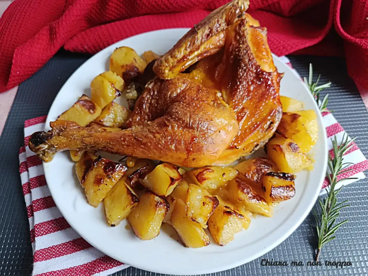 Un succulento pollo e patate al forno, dorati e profumati, serviti su un piatto bianco con un rametto di rosmarino.