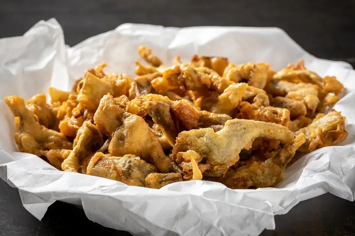 Carci&ograve;fi fritti dorati e croccanti, preparati con una pastella leggera e gustosa, serviti su carta bianca.