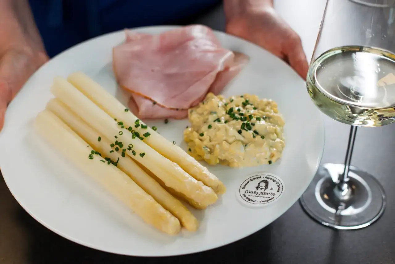Asparagi bianchi con prosciutto e salsa all'uovo, un piatto che ricorda la salsa bolzanina ricetta. Accompagnato da un bicchiere di vino bianco.