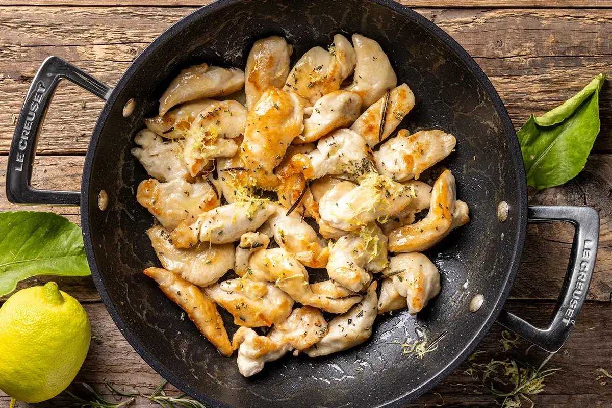 Straccetti di pollo al limone cotti in padella, guarniti con scorza di limone e erbe aromatiche.