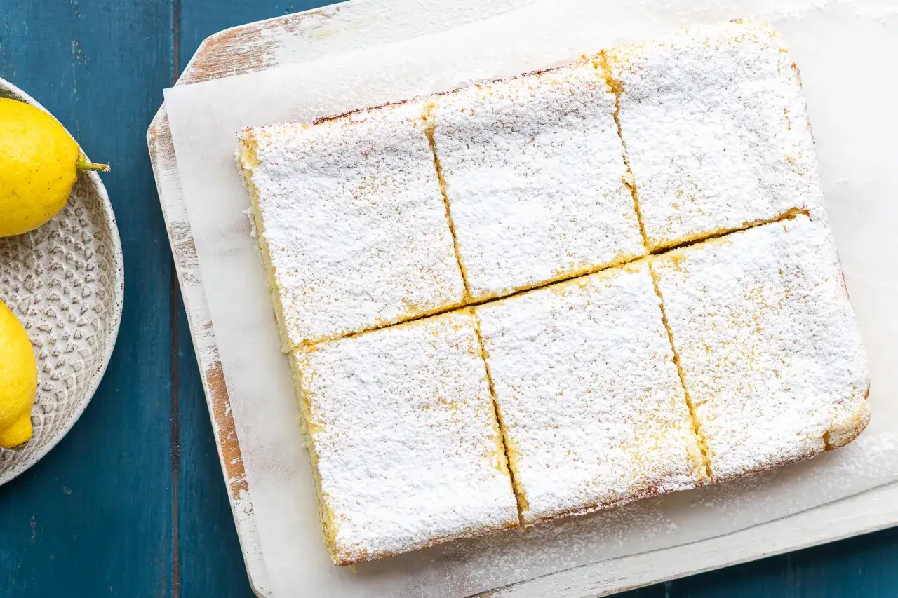 Una torta delle monache, tagliata a quadrotti e cosparsa di zucchero a velo, accanto a limoni freschi.
