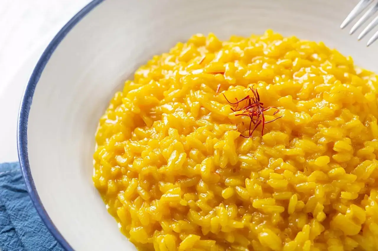 Un cremoso risotto alla milanese, giallo intenso, guarnito con fili di zafferano.