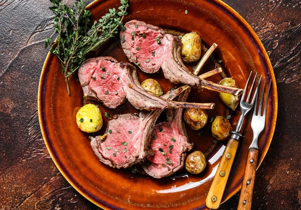 Succulente costolette di agnello cotte alla perfezione, servite con patate arrosto e un rametto di timo su un piatto di terracotta.