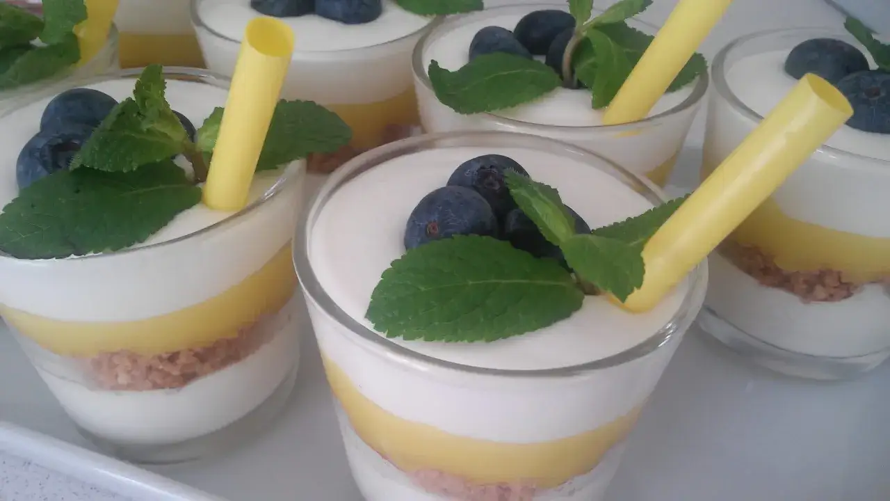 Deliziosi bicchierini con strati di crema, biscotto sbriciolato e una golosa crema al limone, guarniti con mirtilli e menta.