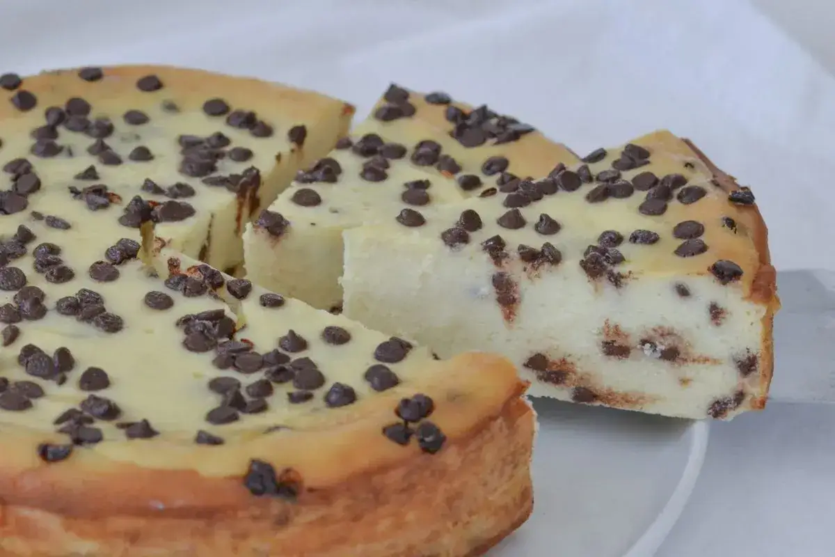 Una deliziosa torta ricotta e cioccolato, con tante gocce di cioccolato sparse sulla superficie e all'interno. Una fetta è appena stata tagliata.