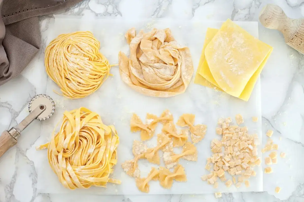 Vari tipi di pasta fresca fatta in casa: tagliatelle, farfalle, sfoglie e maltagliati, pronti per essere cucinati.