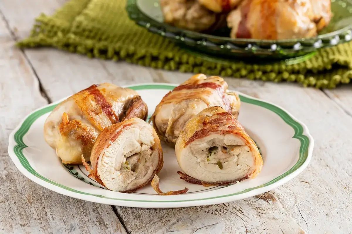 Involtini di pollo succulenti, avvolti in pancetta croccante, serviti su un piatto bianco con bordo verde.